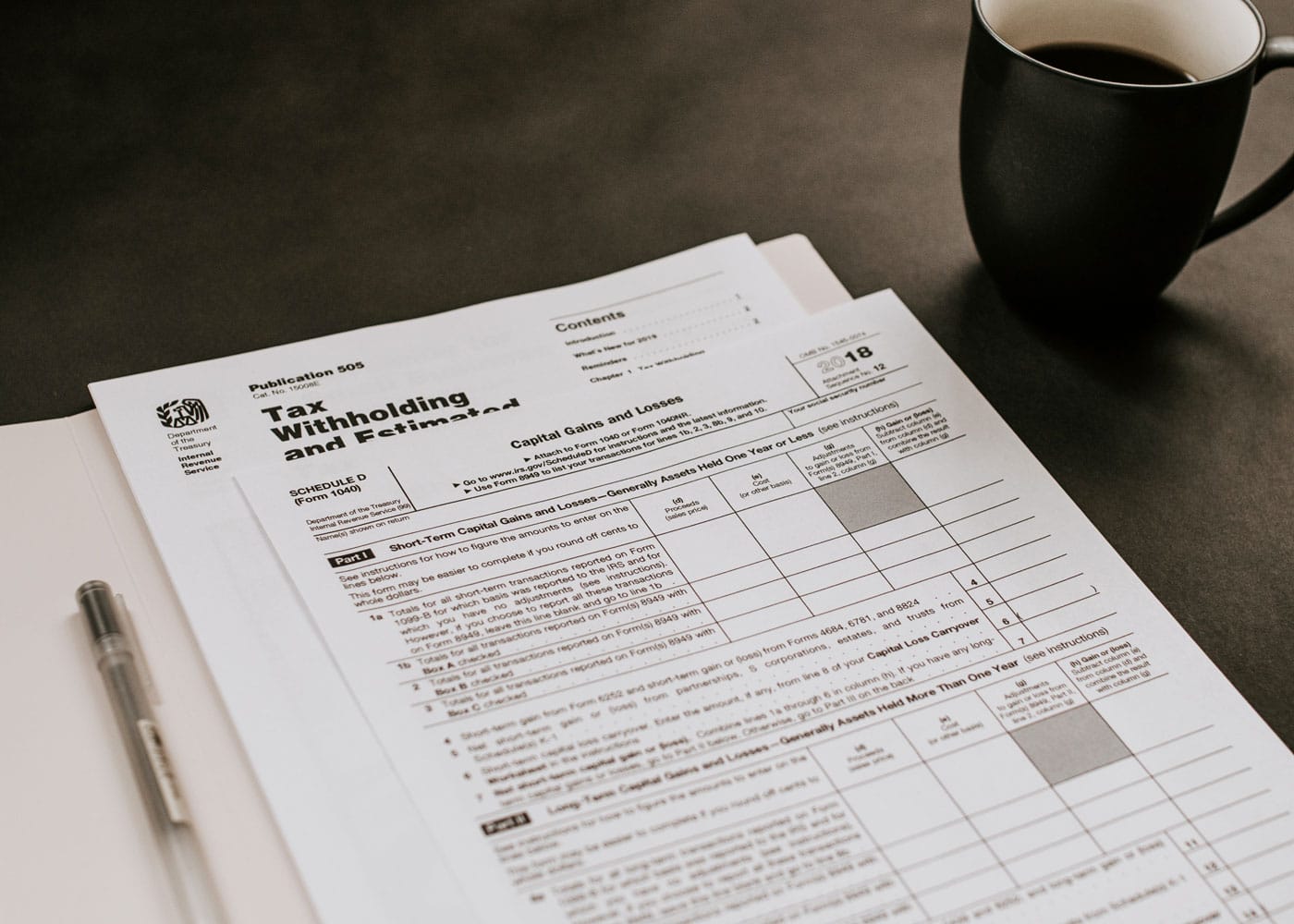 A folder with tax withholding documents, sitting next to a black coffee mug with black coffee