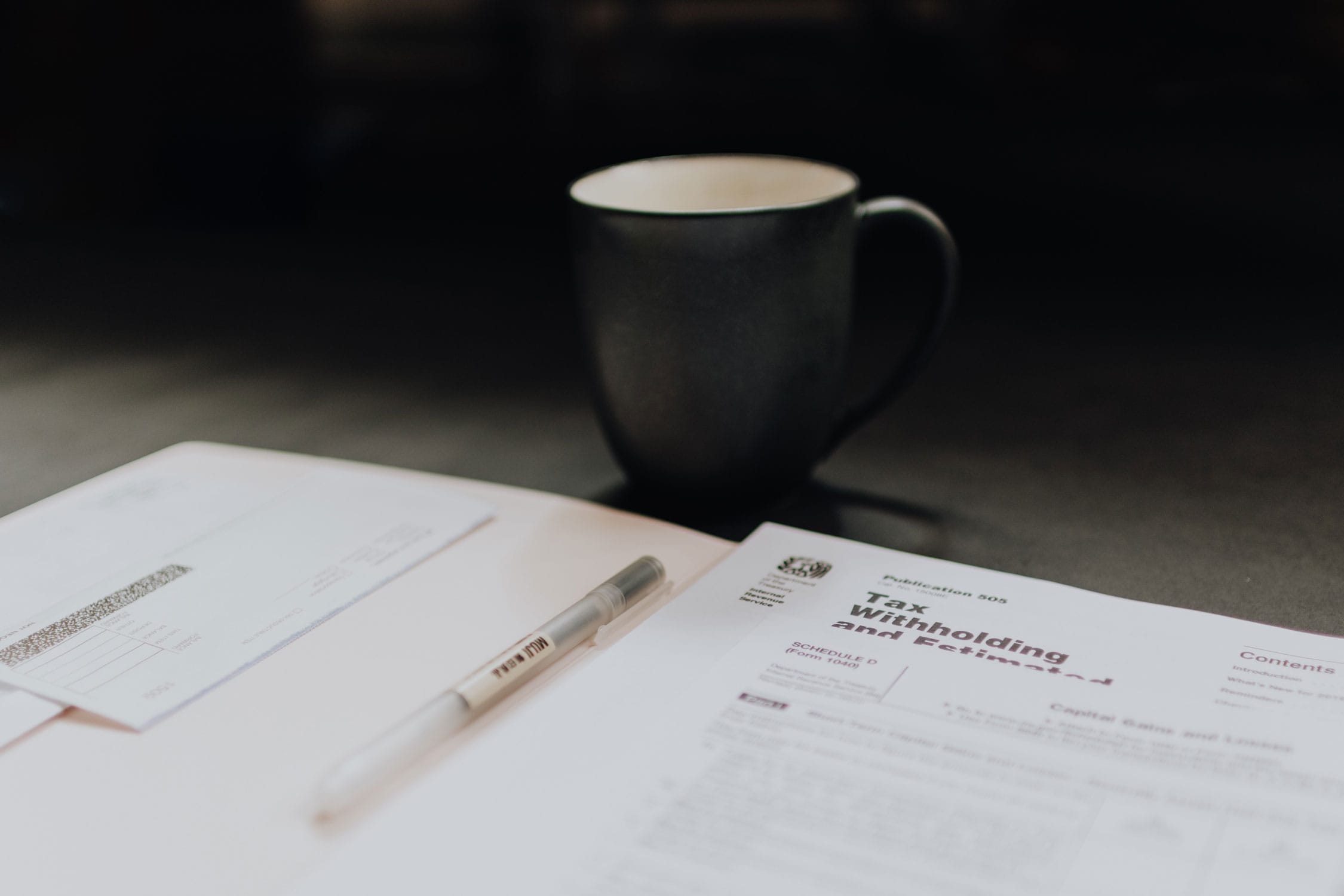 A folder laying on a desk with tax documents and a black coffee mug