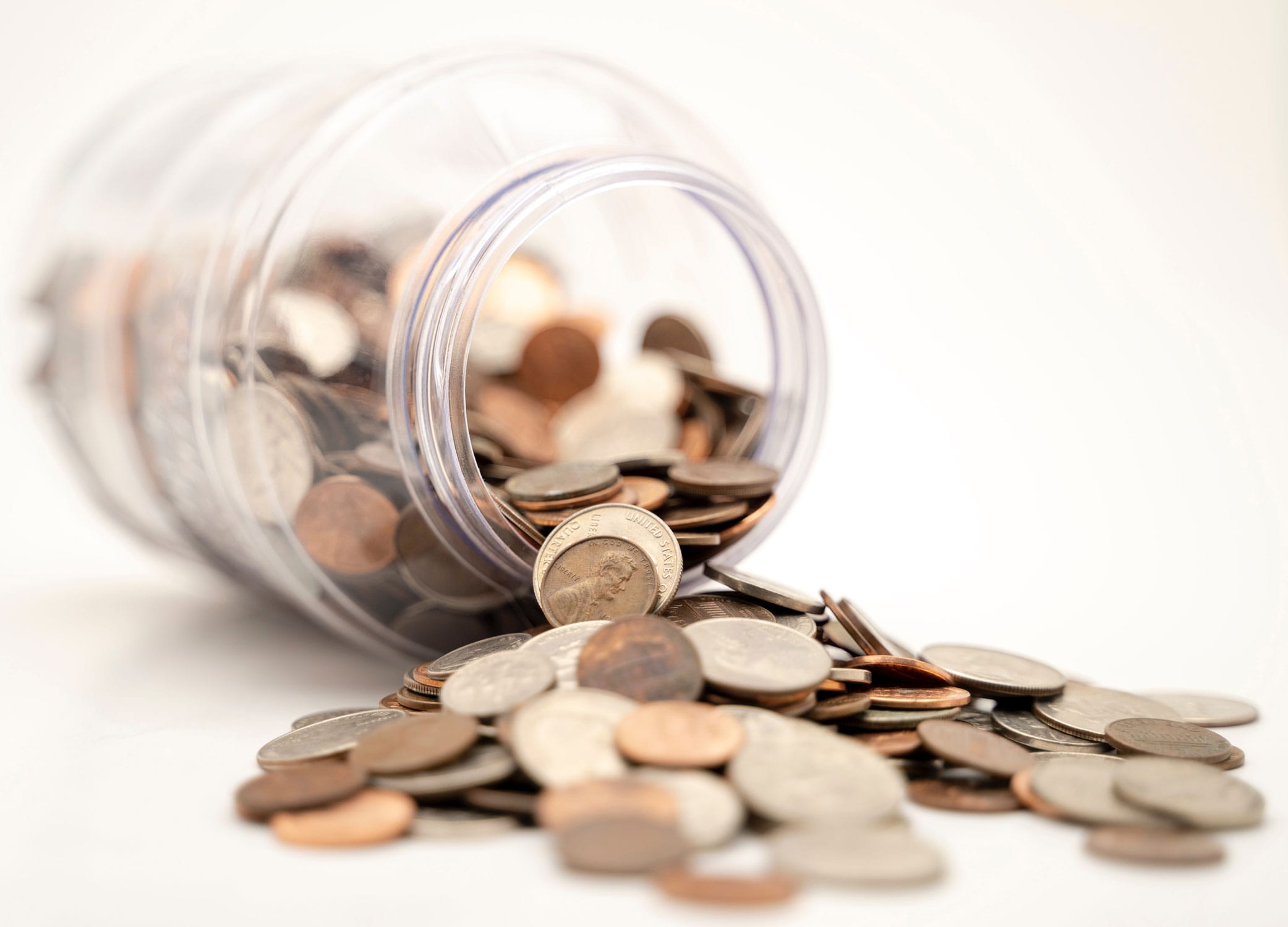 U.S. coins falling out of a clear jar laying on a flat white surface